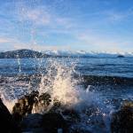 A wave breaks over the rocky shores of Lynn Canal, with Shelter Island and the Chilkat Range seen on the horizon in Southeast Alaska on Dec. 13, 2020. (Courtesy Photo / Sally Thompson)