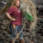 Henry Reiske from the Center for Alaskan Coastal Studies hauls a tangled web of fishing gear and plastic across volcanic rocks. (Ryan Morse / Sitka Conservation Society)