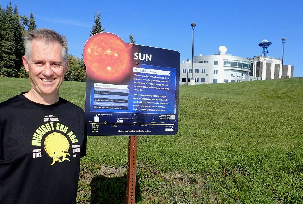 Peter Delamere pauses in front of a UAF Planet Walk sign at the University of Alaska Fairbanks, with the International Arctic Research Center and the Geophysical Institute in the background. (Photo by Ned Rozell)