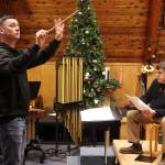 Alan Young (left) conducts while John Cooper reads the words to The Night Before Christmas during a rehearsal Wednesday for holiday concerts by the Taku Winds brass ensemble at K̠unéix̠ Hídi Northern Light United Church. (Mark Sabbatini / Juneau Empire)