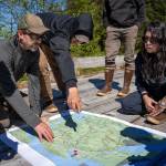 Left to right: Heath Whitacre (U.S. Forest Service), Jason Gubatayao (Sealaska), Khaax̱wáan Dawn Jackson (Organized Village of Kake) sit on the bridge over Yeíl Héeni (Ravens Creek) discussing points on a map of north Kuiu Island. (Photo by Lee House)