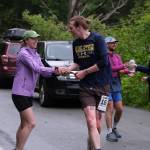 The Stragglers Therese Pokorney and Tim Mikulsi hand off at the Auke Village Recreation Area and Dimond Dogs David Fure gets refreshments during the Seacoast Relay on Sunday, June 8, 2025. (Klas Stolpe / Juneau Empire)