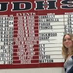 Bella Connally, who just finished her Juneau-Douglas High School: Yadaa.at Kalé freshman track and field season is shown next to her school record for the 100 meters on Wednesday at the JDHS auxiliary gym. (Photo courtesy Chris Connally)