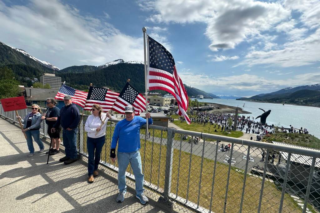 People supporting the U.S. Army on its 250th anniversary gather on the Douglas Bridge on Saturday, June 14, 2025, while a No Kings protest takes place in the backdrop. (Mark Sabbatini / Juneau Empire)